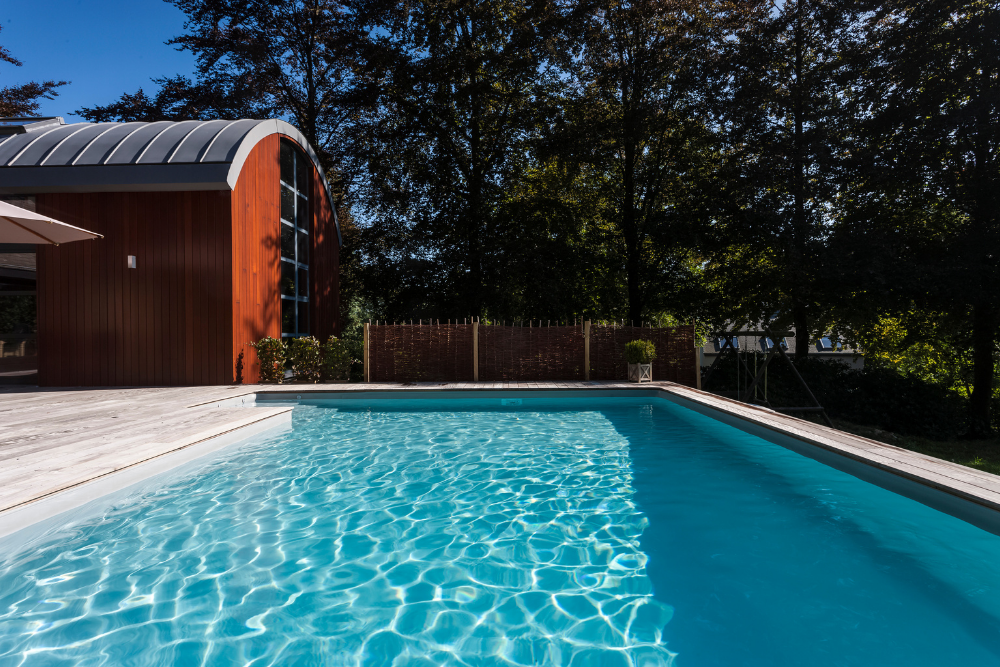 Ein Pool im Garten in der Sonne mit Gartenhaus als Technikraum für eine Wärmepumpe